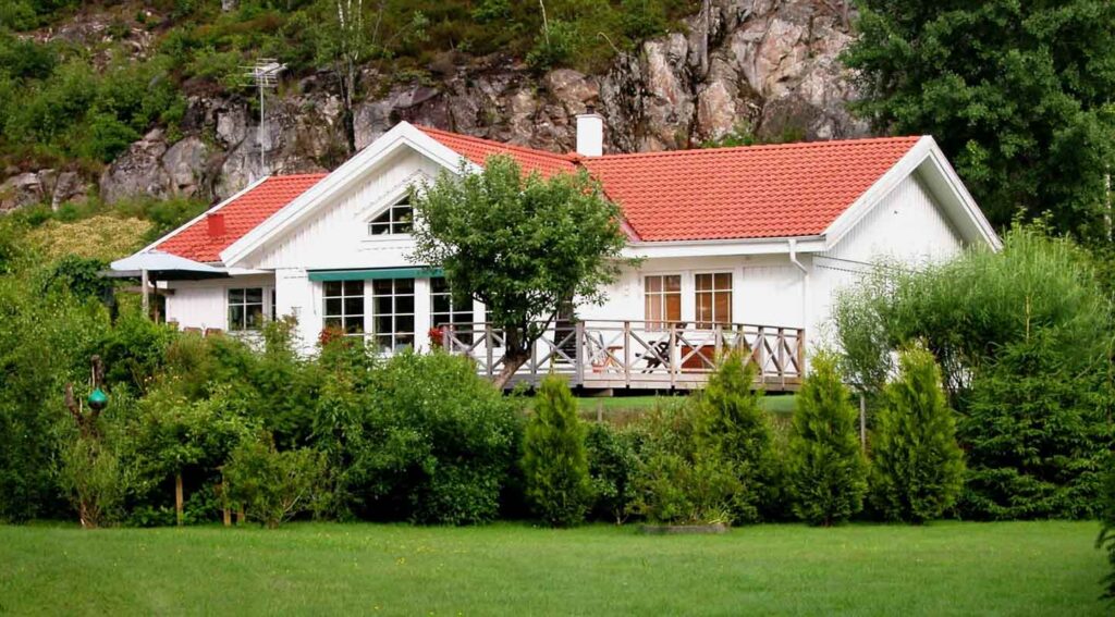 Villa Erika enplanshus bild på fasad med vit stående panel och fönsterpartier fasad med uteplats